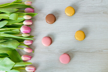 Tulpen mit pinken Blüten liegen auf weißem Holz. Bunte leckere Macarons liegen auf weißem Holz....