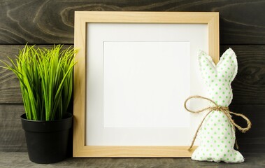 On a wooden background there is a frame for writing text or copying photos and a gentle Easter bunny, a green home flower.  Close-up, front view photograph.  Easter holiday concept.