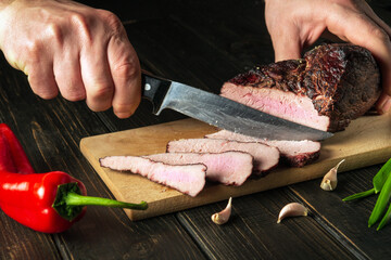 Slicing baked meat on a kitchen board. Close-up of a chef hands with a knife. European cuisine