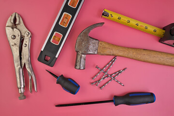 Flatlay of Hand Tools on Pink Background Including Hammer, Nails, Tape Measure, Level, Screwdrivers