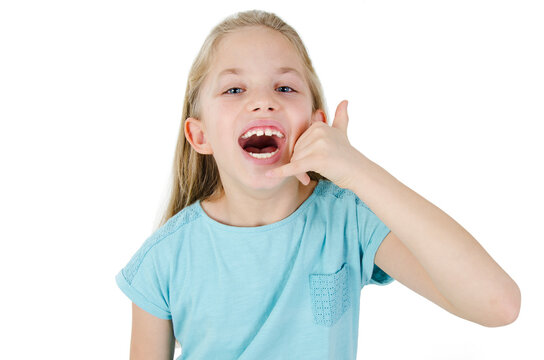 Happy young girl makes call gesture, has satisfied expression, keeps hand near ear, dressed in t shirt, isolated on white background. Adorable beauty girl having fun