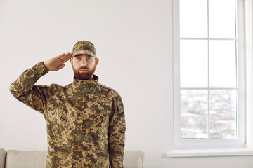 Portrait of male soldier in uniform saluting located indoors at home. Man US officer in military...