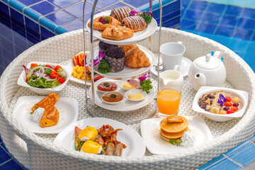 Floating breakfast in luxury hotel resort. Breakfast in swimming pool at villa. Set of served of floating breakfast tray with eggs benedict, salad, fresh fruits and pastry, pancakes, juice, smoothie