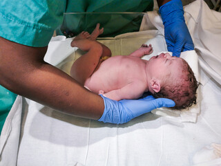 Midwife with african ethnicity are cleaning and treating newborn child at hospital after caesarean...