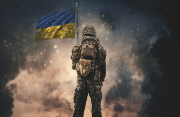 Military soldier with a flag of Ukraine in his hand between smoke and dust at battlefield.