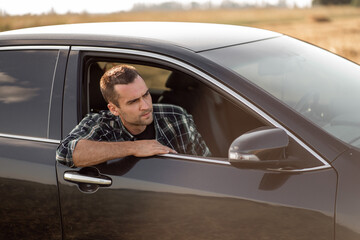 handsome man with short bristles in a checkered shirt looks out the car window