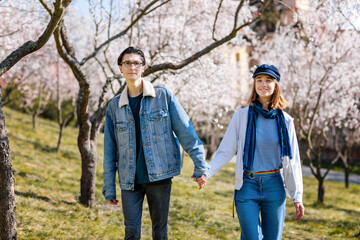 Happy young family lovely couple enjoy walking in spring blooming park, sunny garden on Petrin Hill in Prague, almond and Sakura, close-up portrait, man holds the woman's hand, relationships in love