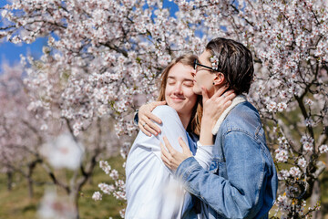 Happy young family lovely couple enjoy walking in spring blooming park, sunny garden on Petrin Hill in Prague, almond and Sakura, close-up portrait, man holds the woman's hand, relationships in love
