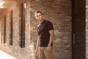 Fototapeta na wymiar handsome man with short bristles in a black T-shirt on a brick wall
