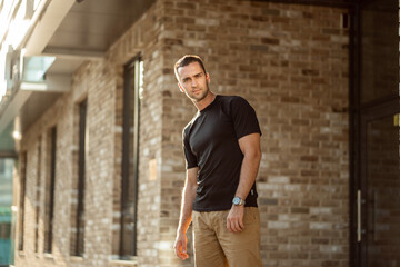 Fototapeta na wymiar handsome man with short bristles in a black T-shirt on a brick wall