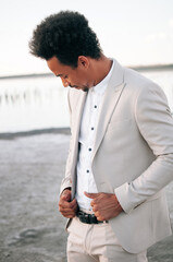 Fototapeta premium Handsome black African American in a light suit. Concept - a man at sunset in a natural place outside the city. Fashion is looking down. Focus on the model's face.