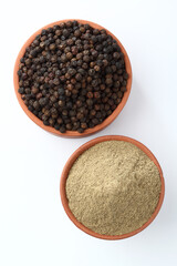 Indian spices Black Pepper powder in a terracotta bowl with pepper corns on white background