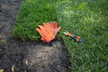 Concept. Work gloves and a lawn clipping knife lie on a roll lawn.
