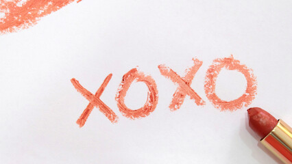The symbol 'XOXO' written on a piece of paper with red lipstick, with the lipstick tube placed next to the word.