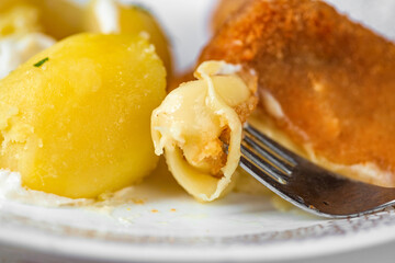 Fried breaded cheese, one piece is melted on fork, boiled potato on plate.