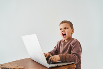 Emotional child with laptop shout. Gambling addiction. Handsome child gamer play online games on laptop on white background.