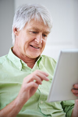 Getting acquainted with technology. Shot of an elderly man using a digital tablet while sitting on the sofa at home.