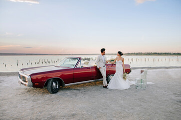 Beautiful couple at sunset on a summer wedding day. Romantic couple in love near their convertible....