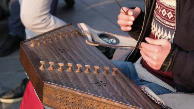 A street musician is playing a hammered dulcimer in slow motion in street. Close-up dulcimer which is a folk musical instrument.