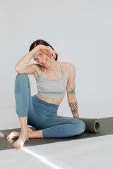 a beautiful girl sits on a rug in a blue-color sportswear. Girl covers her face with her hands