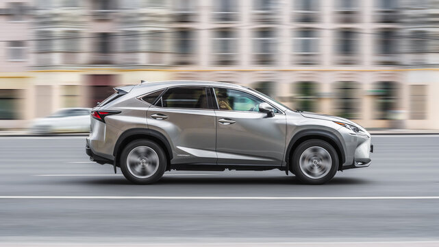 Silver Lexus NX car is moving on city street. Lexus NX 300h driving fast along urban speedway with blurred background