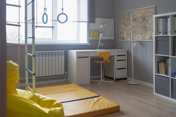 The interior of the room of a boy or girl of schoolchildren with sports equipment, a gymnastic Swedish wall, a yellow armchair with gray walls in light white shades