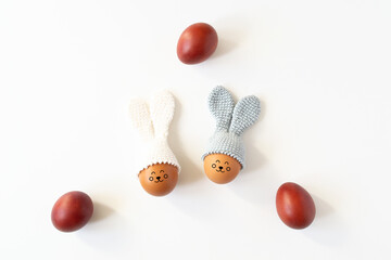 Crocheted Easter eggs with bunny ears and painted red eggs on a white background.