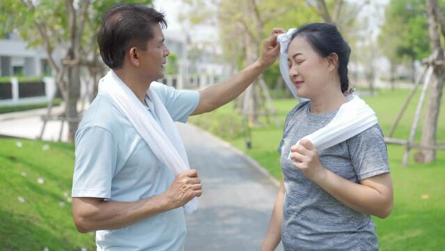Couples wiping sweat while exercising. Asian happy Mature couple husband wiping sweat from face after running at the park.