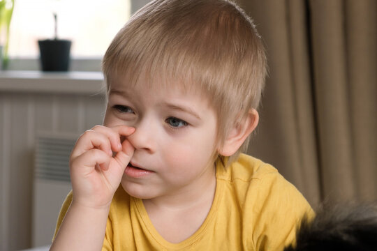 Child boy with blonde hair baby with finger in his nose. Portrait 3 years old kid picking his nose. Boy toddler at home. Early age children education development. Authentic candid lifestyle