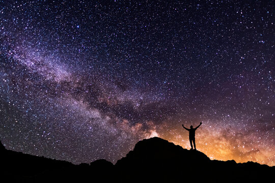 Silhouette of a hiker on the hill in starry night sky.  Bright milky way galaxy behind him.