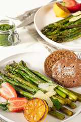 Roasted asparagus with lemon, parmesan and bread serving on a white plate.