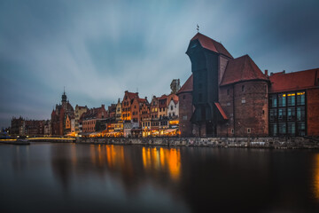 Beautiful architecture of the old town in Gdansk by the Motlawa river with a historic port crane at night. Poland, November 2021