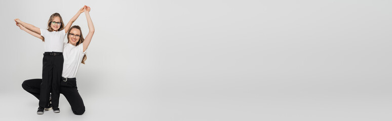 full length view of cheerful mother and daughter holding hands while having fun on grey, banner.