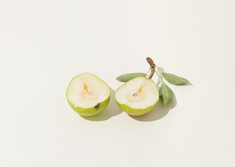 Sunlit halved pear with green leaves standing against isolated pastel white background. Minimal nature summer fruit arrangement. Healthy raw organic food concept. Sun and shadows. 
