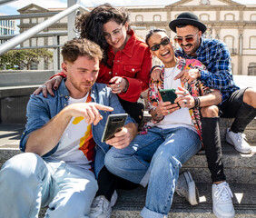 Happy group of multiracial students, friends using smartphone outdoors, watching social media and laughing