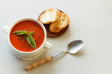 Italian tomato soup with croutons and basil on the table with a spoon.