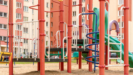 Fototapeta na wymiar children playground attractions of yellow and red colours in dwelling buildings sandy yard close view