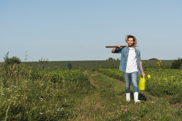 full length view of positive farmer with shovel and watering can walking in field.