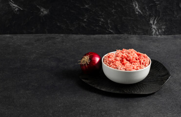 Plate with fresh ground beef, red onion on a gray black background, space for text, stock photo