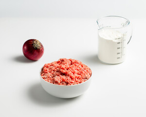 Plate with fresh ground beef, red onion, measuring cup with flour on a white background, stock photo