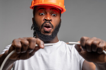 Young electrician in an orange hardhat experimenting with electric wiring