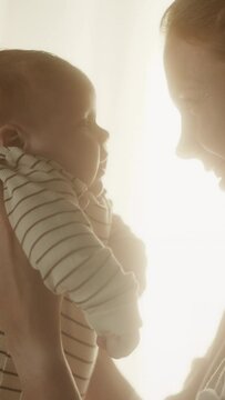 Vertical Format Portrait Video of Happy Mother Holding Cute Newborn Baby in Cozy Dark Kids Bedroom in the Evening. Caring Mom Hugging the Neonate Toddler and They are Bonding Before Sleep.