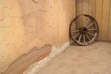 A wagon wheel with several wooden spokes missing
sits in a corner on display