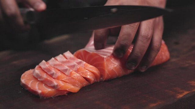 Chef's hand holding fresh piece of salmon.Closeup of chef hands preparing japanese food. Japanese chef making sushi at restaurant.Chef making traditional japanese sushi on wood board.