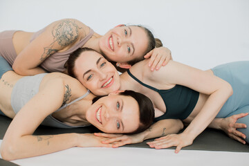 three beautiful women smiling bowed their heads over each other, hugging each other.
girls rest after yoga practice and meditate in a women's circle on a white background