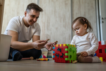 Fototapeta premium baby girl and her father young caucasian man with daughter playing at home happy sitting on the floor with toys in day fatherhood childhood family concept real people copy space