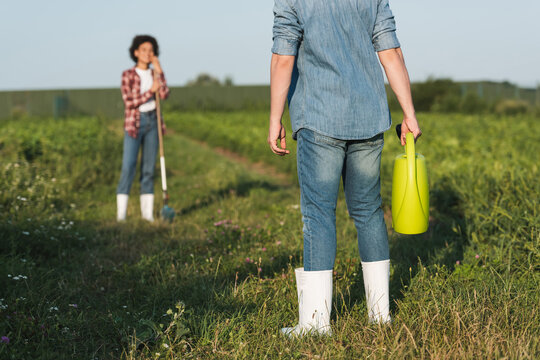 farmer standing with watering can near blurred african american woman.