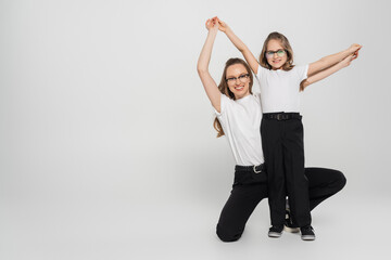 excited girl with mom holding hands and looking at camera while having fun on grey background.