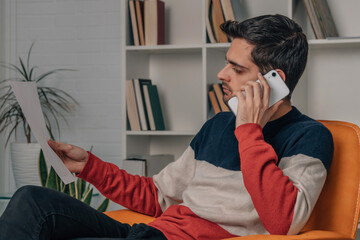 man at home with mobile phone and bill or document