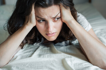 Fototapeta premium Sad, unhappy woman lying on bed in depression. Headache,stress,anxiety,tension,psychological problems. Poor mental health,visiting psychologist,psychotherapy session.Worries about work,family divorce